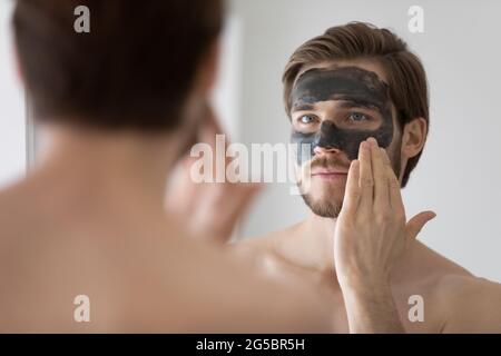 Concentré beau mec métasexuel appliquant l'argile naturelle de nettoyage sombre Banque D'Images