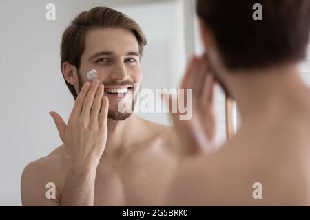 Heureux détendu satisfait beau jeune homme appliquant de la crème de collagène Banque D'Images