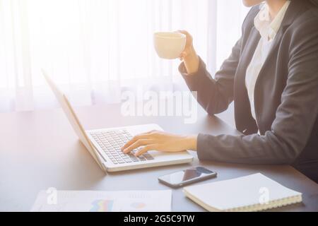 Jeune femme d'affaires utilisant un ordinateur portable sur la table avec une tasse de café à la main, à la recherche de l'orientation et de l'inspiration. Banque D'Images
