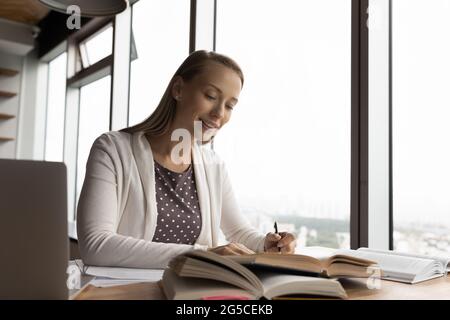 Souriante jeune femme intéressée lisant des livres éducatifs. Banque D'Images