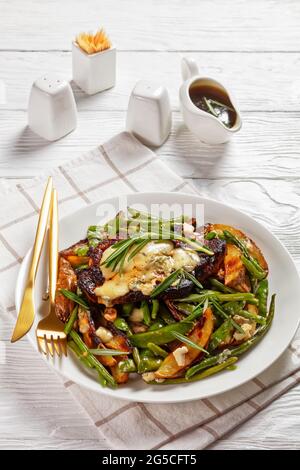 steak de porc recouvert de fromage bleu fondu sur une bande de pois mange-tout grillés, de quartiers de pommes de terre, de haricots verts et d'ail avec sauce trempée dans une sauce b Banque D'Images