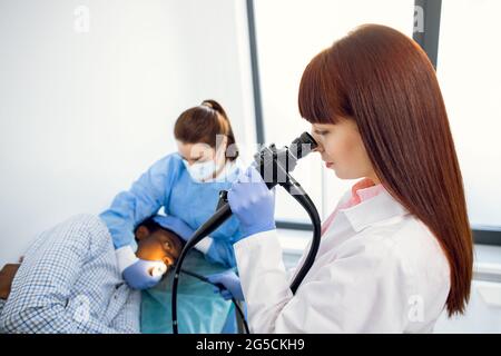 Gastroscopie, endoscopie. Gros plan de la jeune femme professionnelle médecin européen, en regardant dans l'endoscope caméra, tout en faisant l'examen de l'estomac de jeunes hommes africains. Banque D'Images