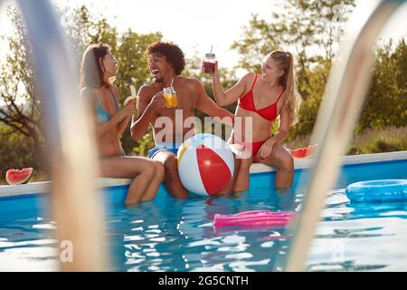 spontané pris moment de jeune afro-américain s'amuser avec deux femelles caucasiennes en plein air dans la nature au bord de la piscine Banque D'Images