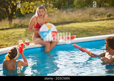 groupe de jeunes adultes s'amusant dans une piscine, jouant avec des pistolets à eau Banque D'Images