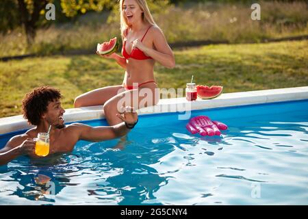 jeune couple multiethnique s'amusant dans la piscine extérieure Banque D'Images