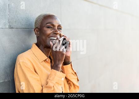 Femme africaine âgée qui fait un appel avec un smartphone mobile tout en fumant de la cigarette Banque D'Images