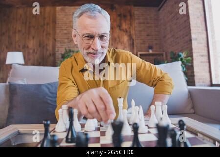 Photo de l'homme aîné gai et élégant jouer aux échecs porter des lunettes jaune chemise à la maison seule Banque D'Images