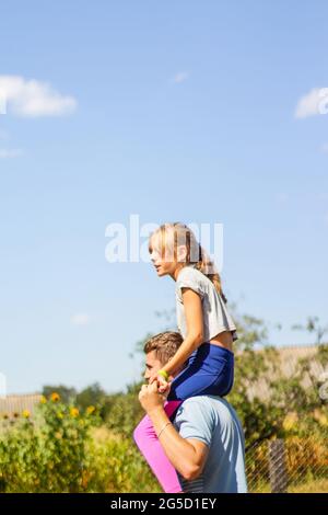 Frère défoqué de la sœur de circonscription à l'arrière. Portrait d'une fille heureuse sur les épaules de l'homme, porcgyback. Petite mouche. Famille jouant à l'extérieur. Arbre bleu ciel vert Banque D'Images