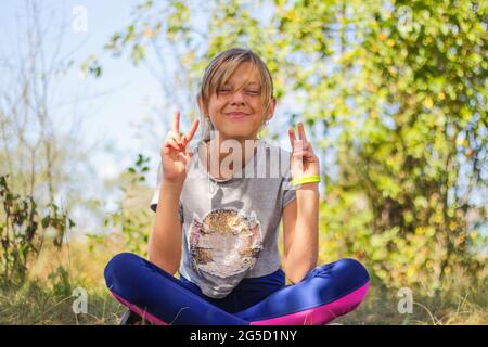 Défocus préadolescence caucasienne pratiquant le yoga dans le parc, la forêt, à l'extérieur, à l'extérieur. S'amuser, montrer des cornes. Bien-être mode de vie sain. Portrait de Banque D'Images