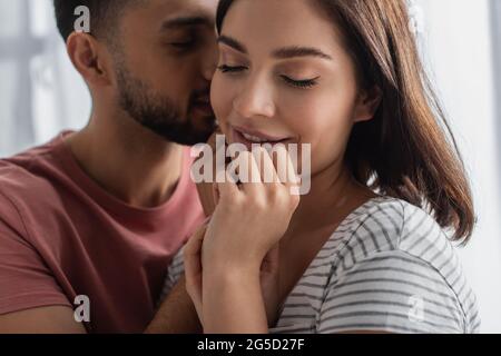 un jeune homme embrasse une petite amie souriante avec les yeux fermés et les mains près du visage dans la cuisine Banque D'Images