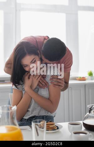 un jeune couple heureux qui se tient près de la table avec le petit déjeuner, le café et le jus d'orange dans la cuisine Banque D'Images