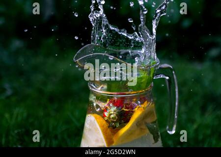 Flou artistique des bulles d'eau dans un verre de limonade avec une tranche de citron, de fraise et de menthe sur fond vert naturel avec des gouttes d'eau. Pichet de Banque D'Images