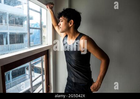 Un jeune et attrayant thaïlandais regarde par les fenêtres de son appartement de Bangkok, Thaïlande. Banque D'Images