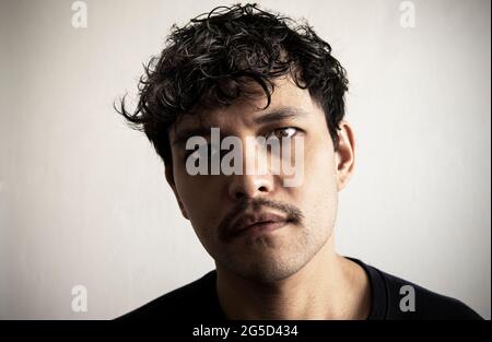 Un jeune homme thaïlandais attrayant avec des cheveux bouclés noirs et une moustache regarde l'appareil photo en portrait. Banque D'Images