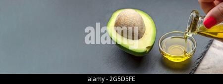 Huile d'avocat. Un avocat avec un os repose sur un plateau en pierre. L'huile d'avocat est versée dans une assiette. Bannière pour l'impression, la conception d'étiquettes, les aliments sains Banque D'Images