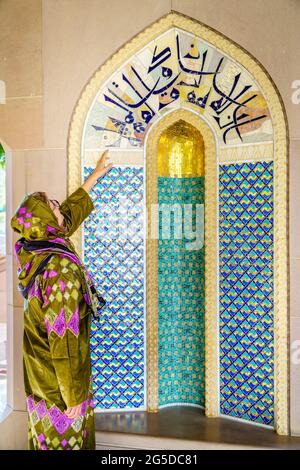 Une femme habillée dans une abaya omanaise traditionnelle qui regarde une alcôve ornée à la grande mosquée du Sultan Qaboos à Muscat, Oman Banque D'Images