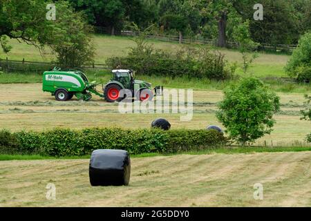 Production de foin ou d'ensilage (agriculteur travaillant dans un tracteur agricole sur une ramasseuse-presse à balles pour le travail dans les champs ruraux, collecte de l'herbe sèche et balles rondes enveloppées - Yorkshire England, Royaume-Uni. Banque D'Images