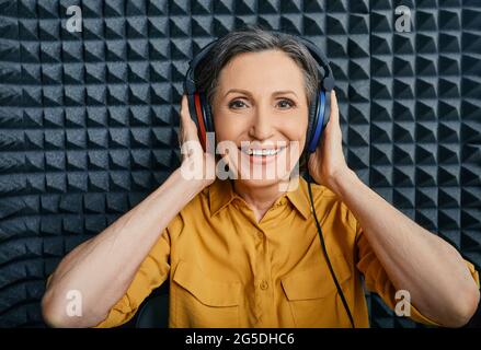 Traitement de la perte auditive. Femme adulte positive portant un casque d'audiométrie pendant un test auditif et un audiogramme dans une salle audio spéciale Banque D'Images