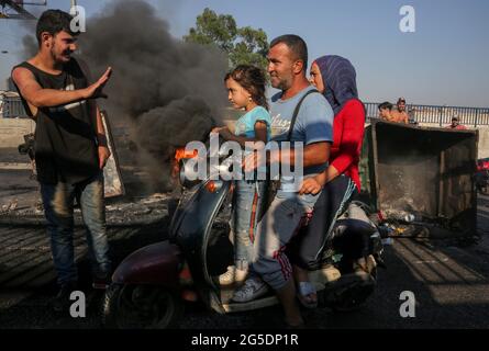 Beyrouth, Liban. 26 juin 2021. Un manifestant se dirige vers une famille qui pilote un scooter alors qu'ils tentent de passer devant une rue bloquée par des pneus en feu lors d'une manifestation anti-gouvernementale contre des conditions de vie difficiles dans un contexte de crise économique et politique en cours. Credit: Marwan Naamani/dpa/Alamy Live News Banque D'Images