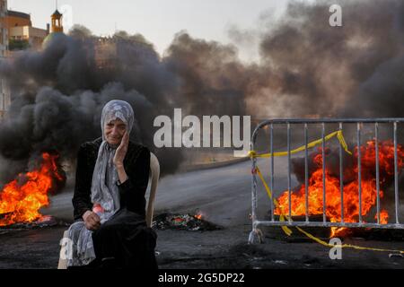 Beyrouth, Liban. 26 juin 2021. Une femme âgée est assise devant des pneus en feu qui bloquent une rue lors d'une manifestation anti-gouvernementale contre des conditions de vie difficiles dans un contexte de crise économique et politique en cours. Credit: Marwan Naamani/dpa/Alamy Live News Banque D'Images