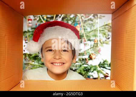 Un garçon souriant regarde dans la boîte à présent portant un chapeau de père Noël Banque D'Images