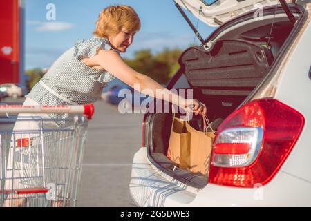 Woman putting de sacs en papier avec de la nourriture dans coffre de voiture Banque D'Images