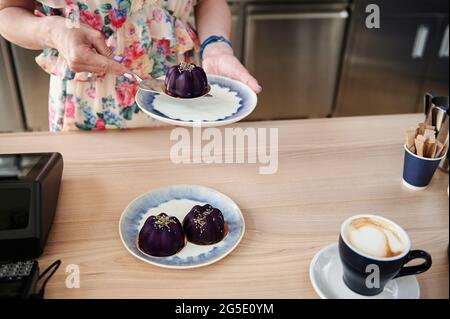 Gros plan des mains de confiserie féminine mettant un délicieux dessert végétalien sur une assiette, debout derrière le comptoir du bar. Les concepts des petites entreprises. Nourriture et Banque D'Images