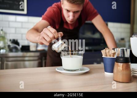 Concentrez-vous sur le fait de verser du café chaud dans du lait fouetté sur un arrière-plan flou du beau jeune barista derrière le comptoir Banque D'Images