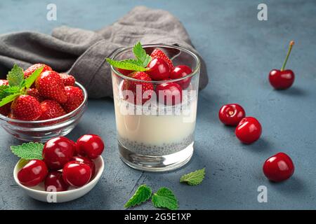 Dessert au lait avec graines de chia et cerises fraîches et fraises sur fond bleu foncé. Banque D'Images