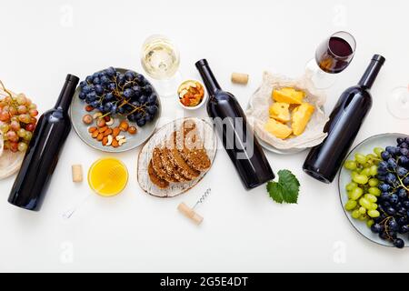 Table de fête servie avec du vin rouge et des en-cas méditerranéens sur fond blanc. Table de dîner avec vin et raisins de fromage Banque D'Images