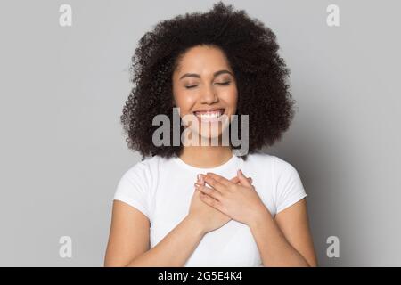 Une femme afro-américaine souriante tient les mains sur la poitrine Banque D'Images