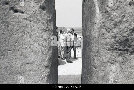 Années 1960, historique, vue à travers un écart entre deux pierres de visiteurs à l'ancienne pierres de Stonehenge, Wiltshire, Angleterre, Royaume-Uni.à ce moment on pouvait marcher librement autour des pierres préhistoriques mais dans la décennie suivante en raison du nombre de visiteurs, des dommages à l'herbe et de l'érosion au sacré, ancien site de sépulture, les pierres ont été pillées pour empêcher l'accès. Situé sur le domaine de l'abbaye d'Amesbury, propriété à une époque du roi Henri VIII, Cecil Chubb a apporté la parcelle de terre avec les pierres lors d'une vente aux enchères en 1915 et en 1918 l'a donné à la nation britannique. Banque D'Images