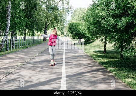 Enfants à faire du skateboard dans le parc d'été. Petite fille apprenant à monter sur le skateboard. Sports d'extérieur actifs pour les écoliers. Skateboard pour enfants. Banque D'Images