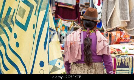 Femme indigène équatorienne Otavalo en vêtements traditionnels, chapeau et coiffure sur le marché local Otavalo avec des étals de textile et de tissu, Équateur. Banque D'Images