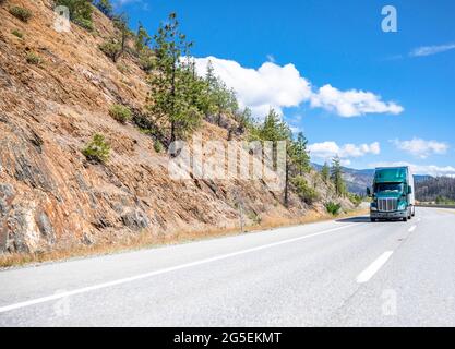 Capot vert classique puissant tracteur semi-remorque industriel long-courriers transportant des charges commerciales dans une remorque semi-remorque à fourgon sec en montée Banque D'Images