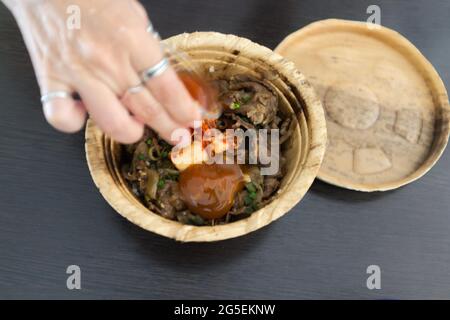 Femme main avec le gyudon japonais avec oeuf ou bol de boeuf japonais avec oeuf dans bol de feuille de banan biologique Banque D'Images