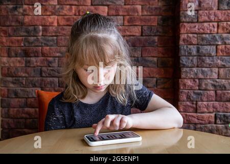 Une petite fille apprend des notes de manière ludique, avec l'aide d'un piano sur son téléphone. Banque D'Images