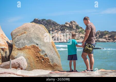 Papa se soucie de son près de la mer, marcher passer du temps ensemble explorer nouveau. Un homme tient la main d'un enfant, regarde vers le bas. Nature mer rock. Élever garçon, père Union familiale Banque D'Images
