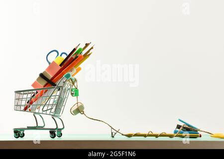 Concept d'achat avec chariot d'achat avec fournitures scolaires sur le dessus et de tirer des outils accrochés à une corde sur fond vert. Vue de dessus. Position horizontale Banque D'Images