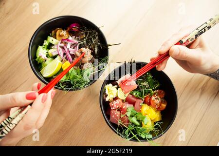 Homme et femme mangeant de la salade de poke avec des baguettes. Verser la salade de thon dans un bol. Les gens du restaurant mangent de la salade avec des baguettes. Salade de fruits de mer asiatiques Banque D'Images