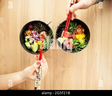 Homme et femme mangeant de la salade de poke avec des baguettes. Verser la salade de thon dans un bol. Les gens du restaurant mangent de la salade avec des baguettes. Salade de fruits de mer asiatiques Banque D'Images