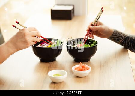 Homme et femme mangeant de la salade de poke avec des baguettes. Verser la salade de thon dans un bol. Les gens du restaurant mangent de la salade avec des baguettes. Salade de fruits de mer asiatiques Banque D'Images