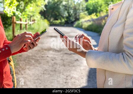 Gros plan de deux mains de filles utilisant leur smartphone dans un parc. Une fille porte une veste blanche et l'autre un chandail rouge. Une voie de campagne sur l'île de ba Banque D'Images