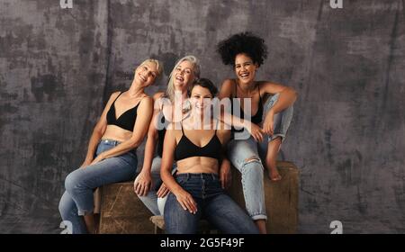 Photo courte de femmes diverses qui rient ensemble. Quatre femmes positives de corps de différents âges célébrant leur corps naturel tout en portant de nouveau des jeans Banque D'Images