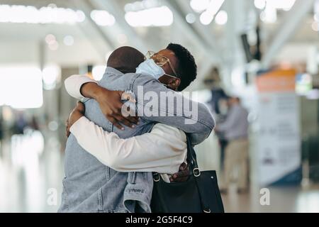 Couple de voyageurs africains lors d'une réunion pandémique à l'aéroport. Homme au terminal de l'aéroport embrassant une femme avec un masque facial avant le départ. Banque D'Images