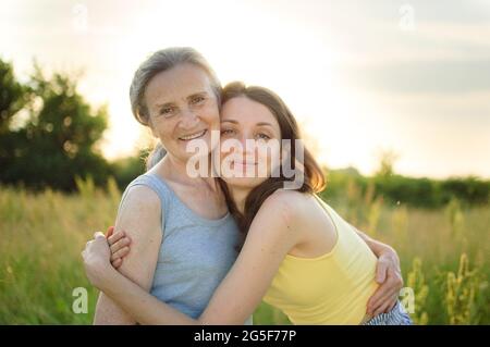 Mère âgée aux cheveux gris avec sa fille adulte à la caméra dans le jardin et se embrassant pendant la journée ensoleillée à l'extérieur Banque D'Images