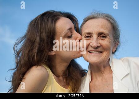 Mère âgée aux cheveux gris avec sa fille adulte à la caméra dans le jardin et se embrassant pendant la journée ensoleillée à l'extérieur Banque D'Images