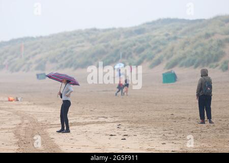 Camber, East Sussex, Royaume-Uni. 27 juin 2021. Météo au Royaume-Uni : le temps pluvieux attendu plus tard est arrivé tôt sur les plages de sable de Camber Sands dans l'est du Sussex. Certaines familles ont l'intention de profiter de la journée lorsqu'elles arrivent avec des parasols et des ponchos de pluie. Crédit photo : Paul Lawrenson /Alay Live News Banque D'Images