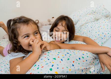 Deux jeunes filles de race blanche, âgées de deux et neuf ans, s'amusent ensemble sur leurs lits, jouant et parlant. Banque D'Images