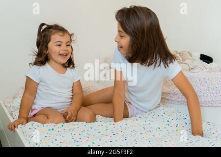 Deux jeunes filles de race blanche, âgées de deux et neuf ans, s'amusent ensemble sur leurs lits, jouant et parlant. Banque D'Images